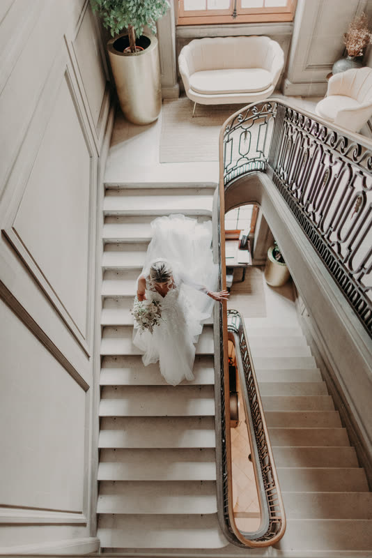 La mariée descend l'escalier, bouquet blanc à la main
