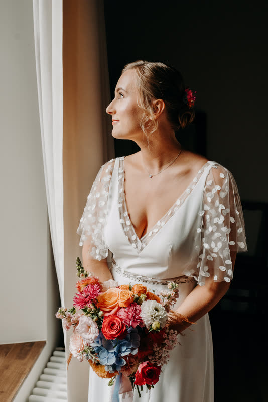 La mariée et son bouquet coloré près d'une fenêtre
