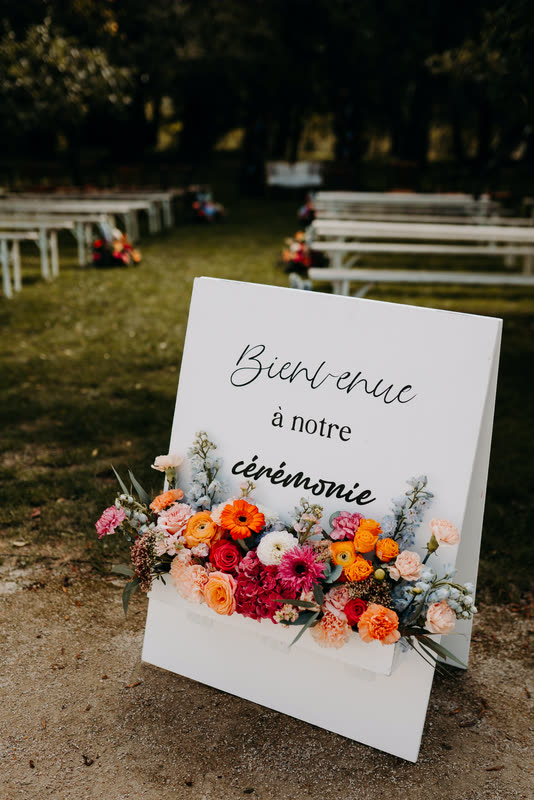 Panneau de bienvenue posé au sol et entouré de fleurs colorées