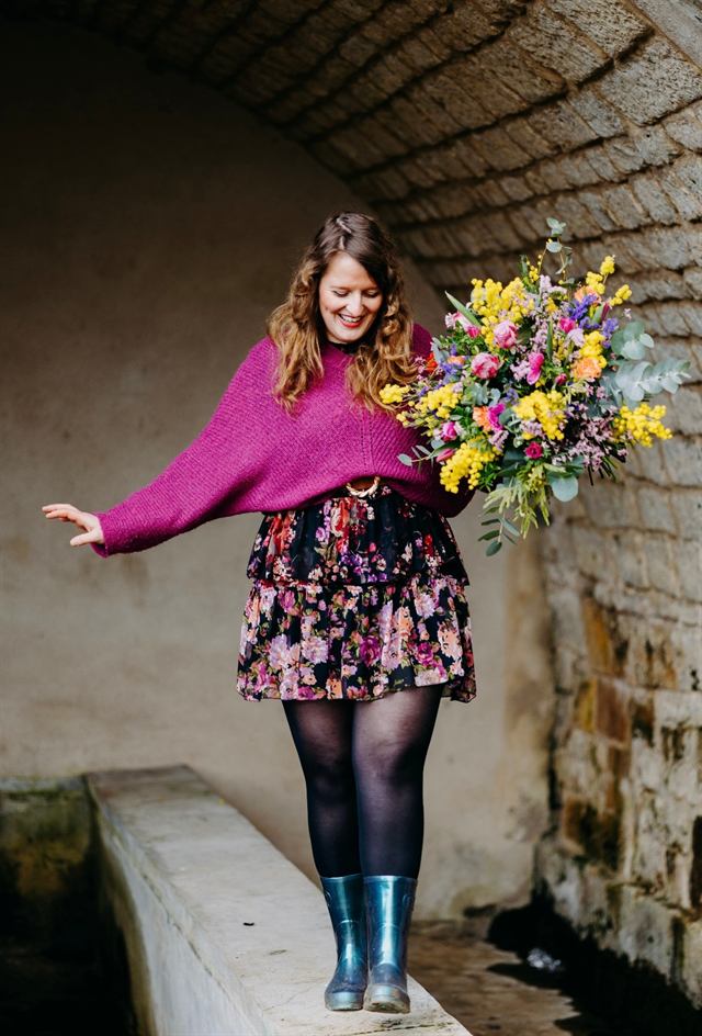 Pauline Wilmouth sous une voûte en pierre, un grand bouquet de mimosa à la main